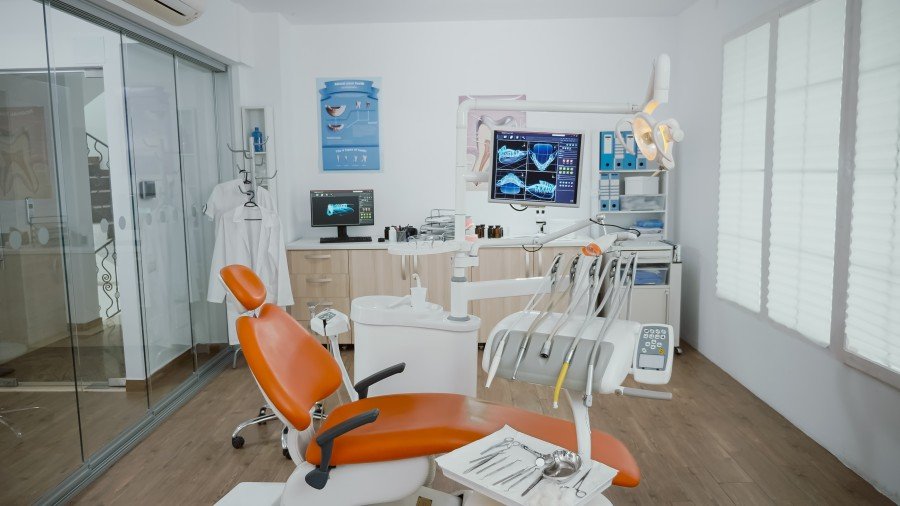 Bright, modern dental office with an orange dental chair, examination equipment, monitors, and instruments.