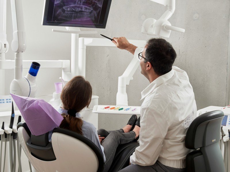 Dentist showing a patient a dental X-ray on a monitor during a consultation.
