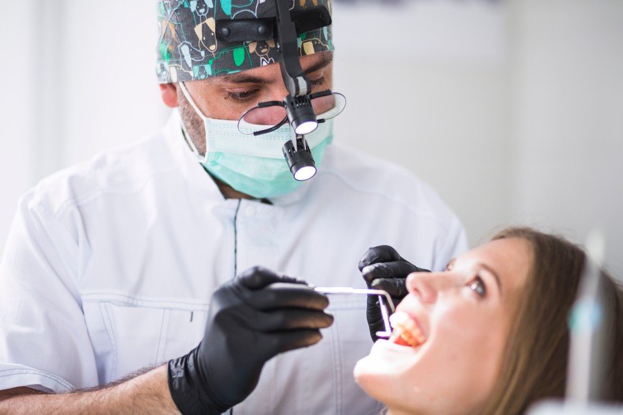 Dentist examining a female patient’s teeth with dental instruments in a clinic.