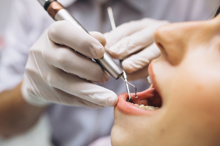 Dentist examining a patient’s teeth with a dental instrument while wearing gloves.